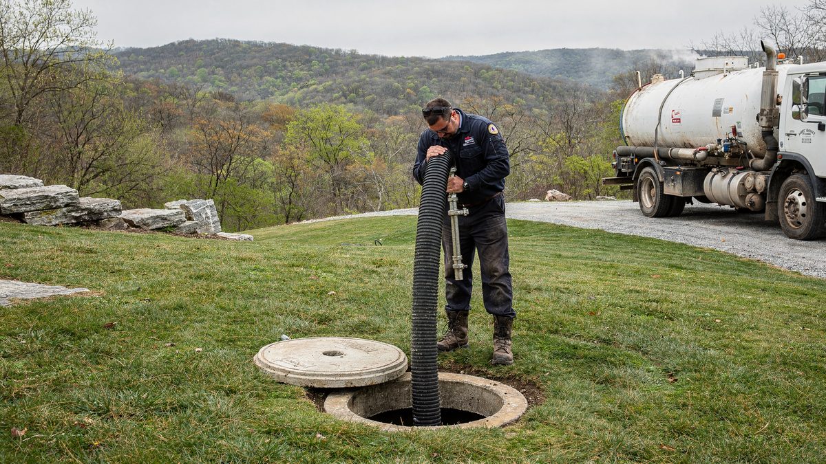 Vacuum tanker staged on a gravel drive while a technician draws down a septic tank on a call outside Springfield, Missouri